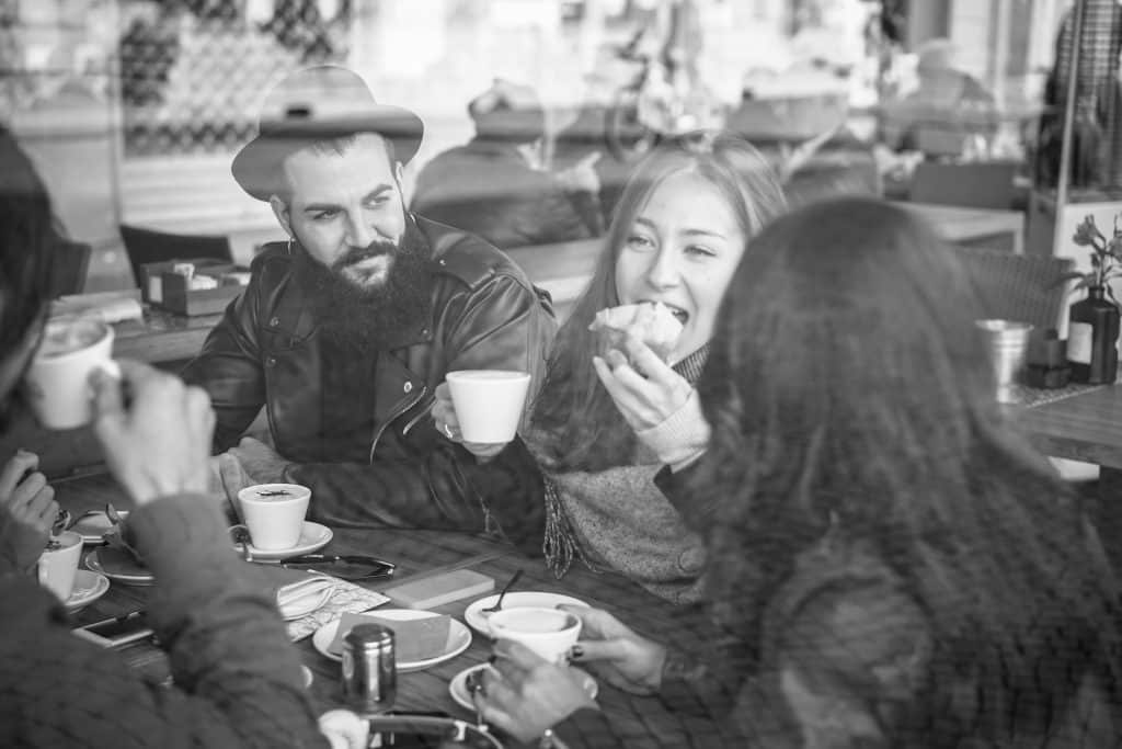 Fröhliche Freunde, die in der Cafeteria einer Bar frühstücken und Milchkaffee trinken