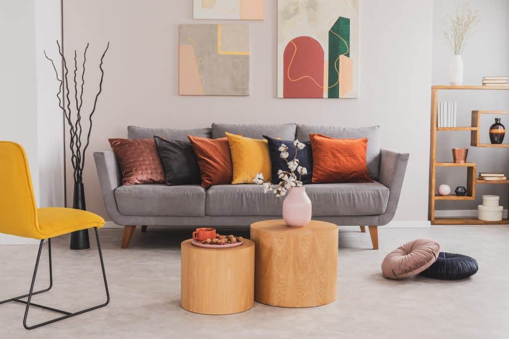 Neubau Berlin: Echtes Foto von runden Holztischen, die vor einem grauen Sofa mit bunten Kissen in einem hellen Wohnzimmer stehen
