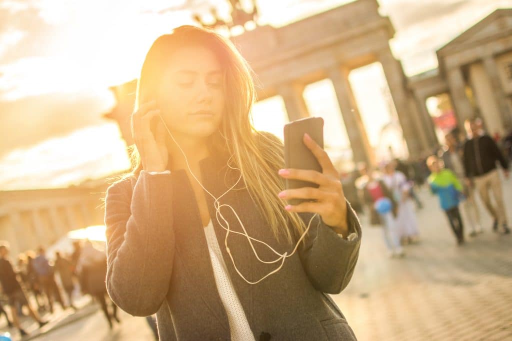 Eine junge Frau hört beim Spaziergang in der Nähe des Brandenburger Tors in Berlin bei Sonnenuntergang Musik auf ihrem Handy.