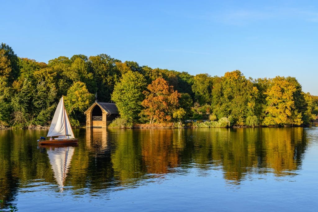 Berlin district of Steglitz: Natural landscape view of forest with autumn leaves in Pfaueninsel island and boat sail at Wannsee lake,  Havel river