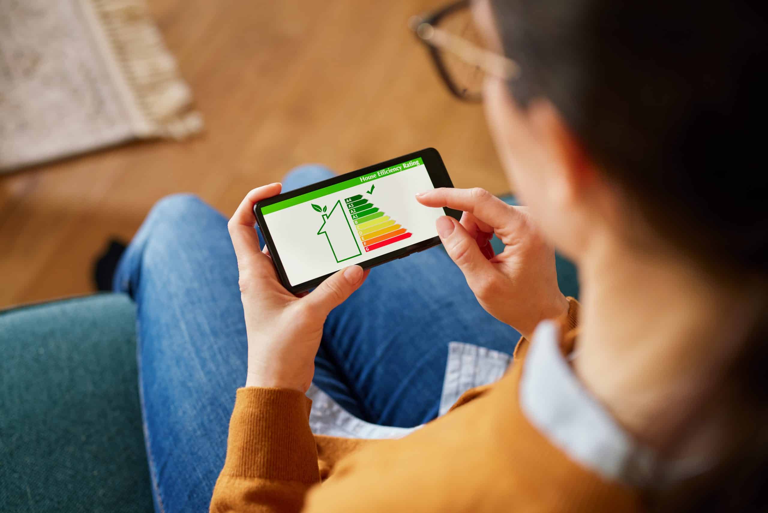 Eine Frau überprüft die Energieeffizienzklasse ihrer Wohnung auf ihrem Smartphone. Sie sieht sich die Energiesparpotenziale der Wohnung auf dem Bildschirm ihres Handys an.