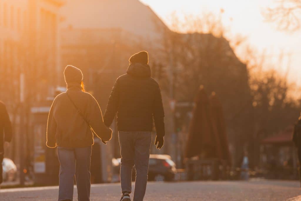 Paar spaziert Hand in Hand die Berliner Allee entlang in den orangefarbenen Sonnenuntergang, bei kühlem, sonnigem Frühlingswetter