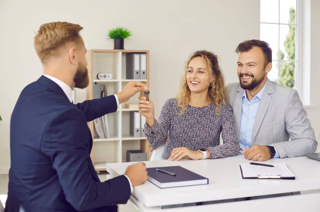 Wohnung kaufen Berlin Prenzlauer Berg: 
Ein Immobilienmakler übergibt einem begeisterten Ehepaar bei einem Termin in seinem Büro die Schlüssel zu dessen neuem Zuhause.
