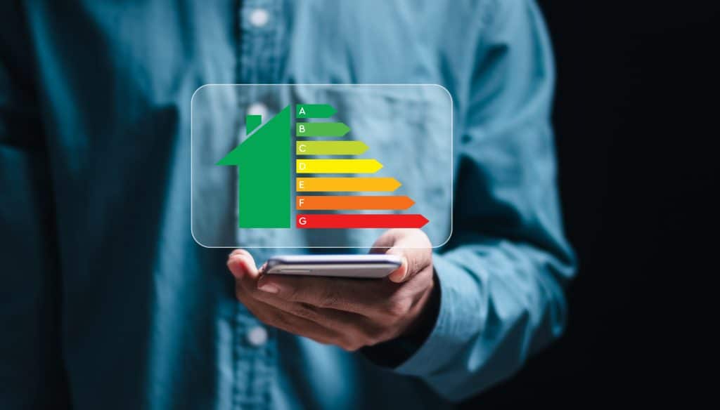 Energieeffizienzkonzept. Eine Person nutzt ein Smartphone mit einer virtuellen Anzeige der Energieeffizienzklasse zur Überprüfung des Energieeffizienz-Gütesiegels für energieeffiziente Gebäude.